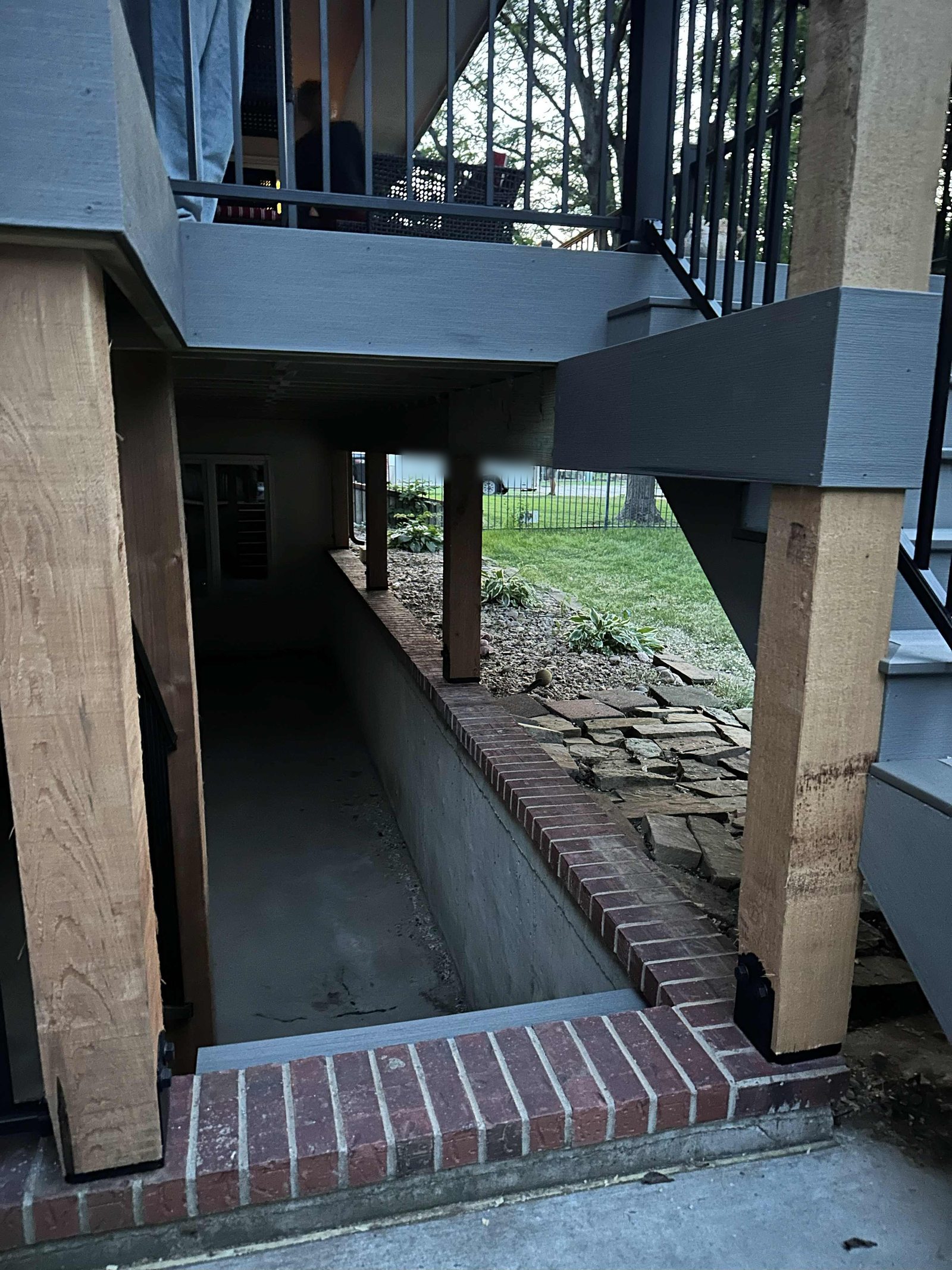 Rough-sawn posts on steel bases set on the brick stairwell wall below the deck