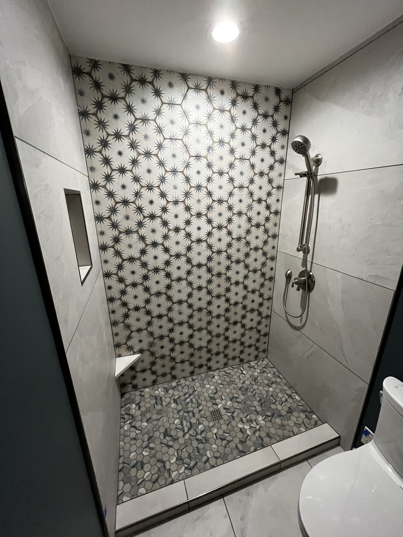 Tiled walk-in shower with pebble floor and patterned accent wall